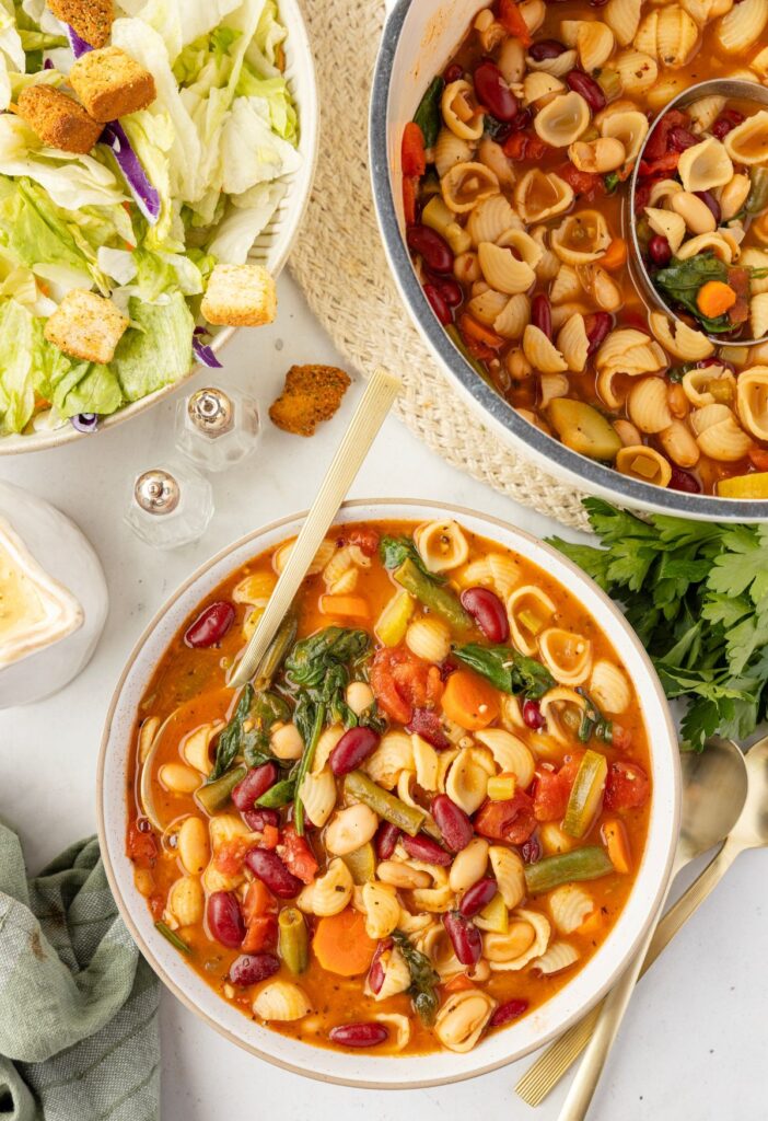 Pot of soup with a serving bowl of it inside a bowl, a bowl of salad to the side. 