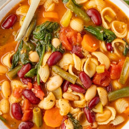 A bowl of veggie loaded minestrone soup with a gold spoon.