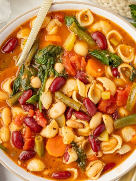 A bowl of veggie loaded minestrone soup with a gold spoon.