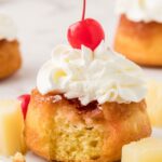 A pineapple upside down cupcake with whipped cream and a cherry on top, a fork bite taken out of the front of it.