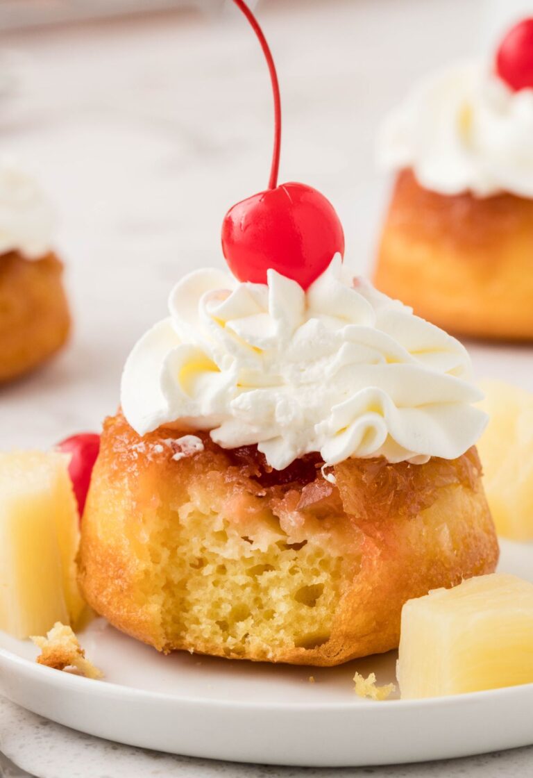 A pineapple upside down cupcake with whipped cream and a cherry on top, a fork bite taken out of the front of it.