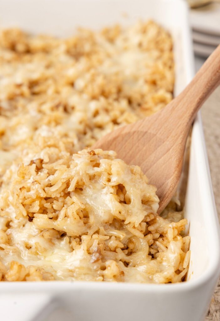 A wooden spoon with some baked rice on top of it and melted gruyere cheese