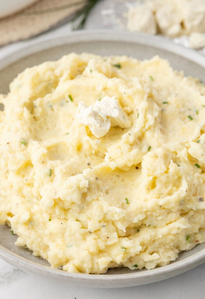 A bowl of mashed potatoes with Boursin cheese chunks on top. 