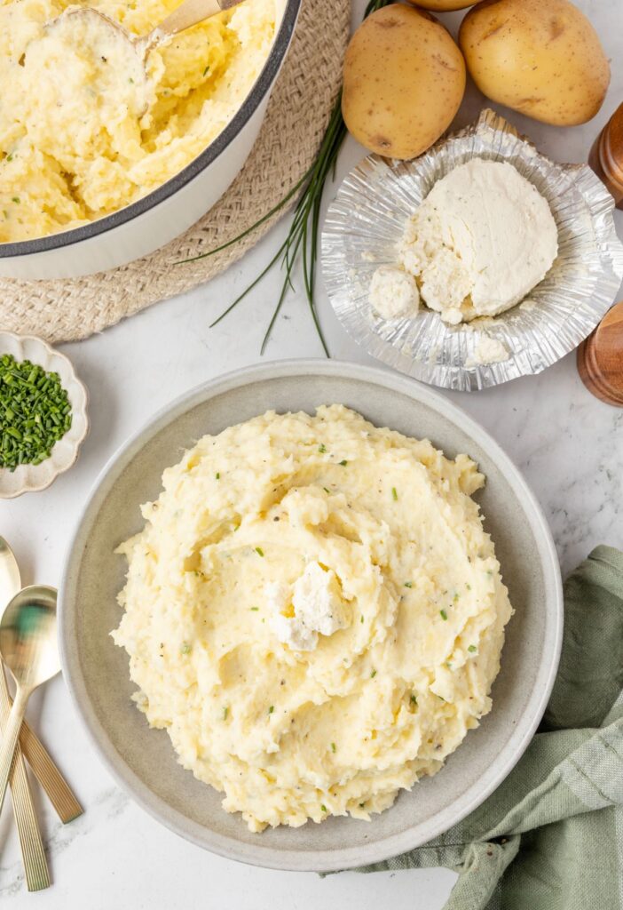 Serving of mashed potatoes with a Boursin cheese wedge to the side and salt and pepper. 