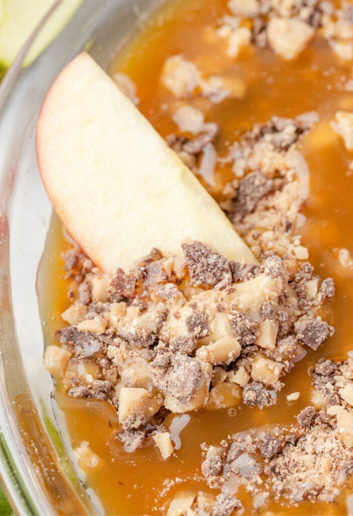 An apple slice inside the caramel apple fruit dip in a pie plate. 