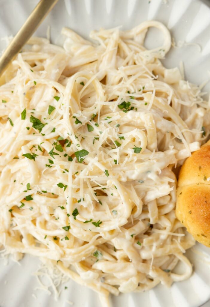 A white plate with a serving of cream cheese pasta on it. 