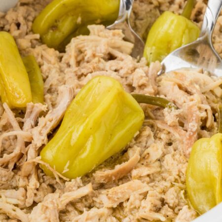 Close up of the shredded chicken inside the crockpot with pepperoncini peppers