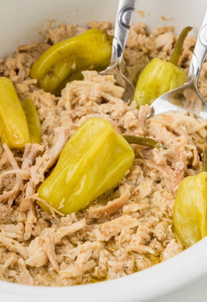 Close up of the shredded chicken inside the crockpot with pepperoncini peppers