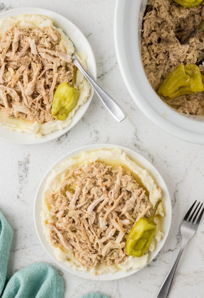 Top view of servings of the Mississippi chicken with the crockpot full of the shredded chicken in it. 