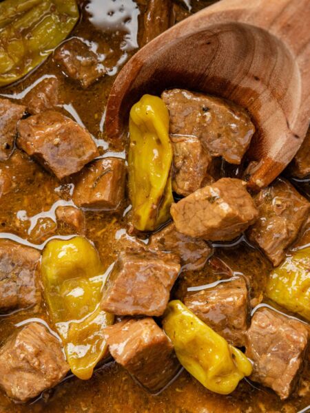 Close up of the steak bites on a wooden spoon inside the slow cooker.