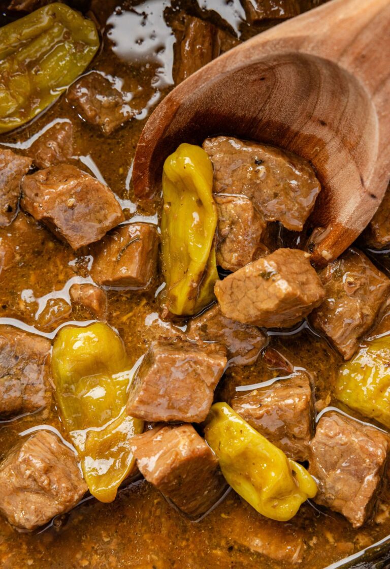 Close up of the steak bites on a wooden spoon inside the slow cooker.
