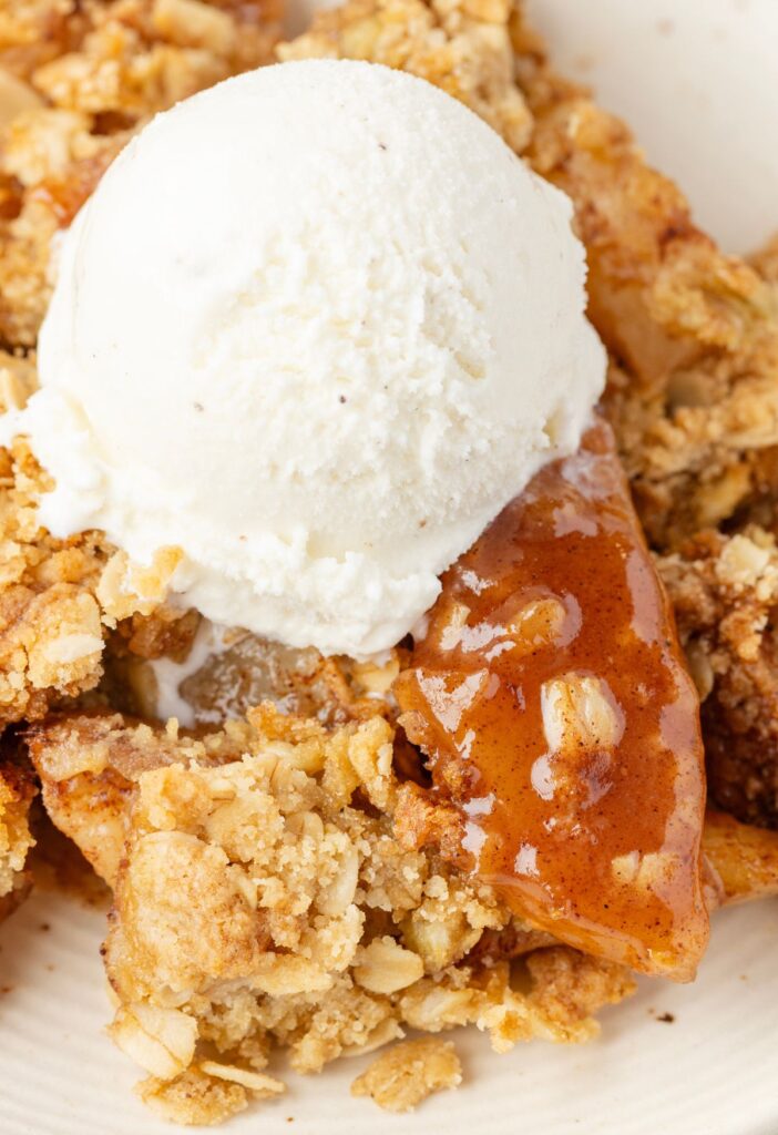 Close up of a serving of pear crisp with vanilla ice cream over top of it. 