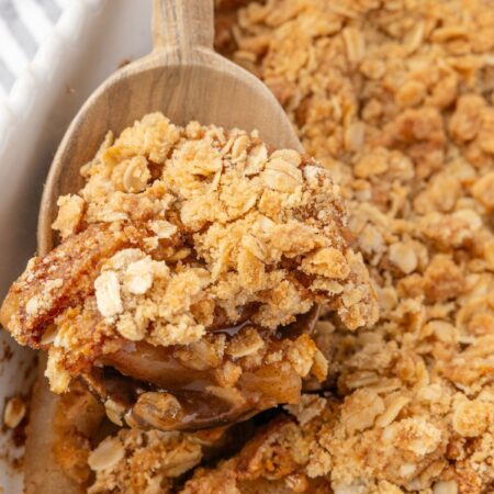 A wooden spoon holding some pear crisp on it above the pan of the fruit crisp.