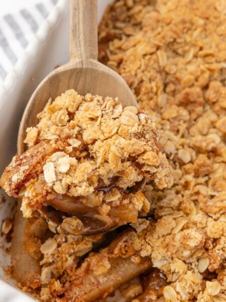 A wooden spoon holding some pear crisp on it above the pan of the fruit crisp.