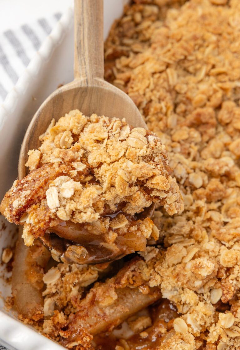 A wooden spoon holding some pear crisp on it above the pan of the fruit crisp.