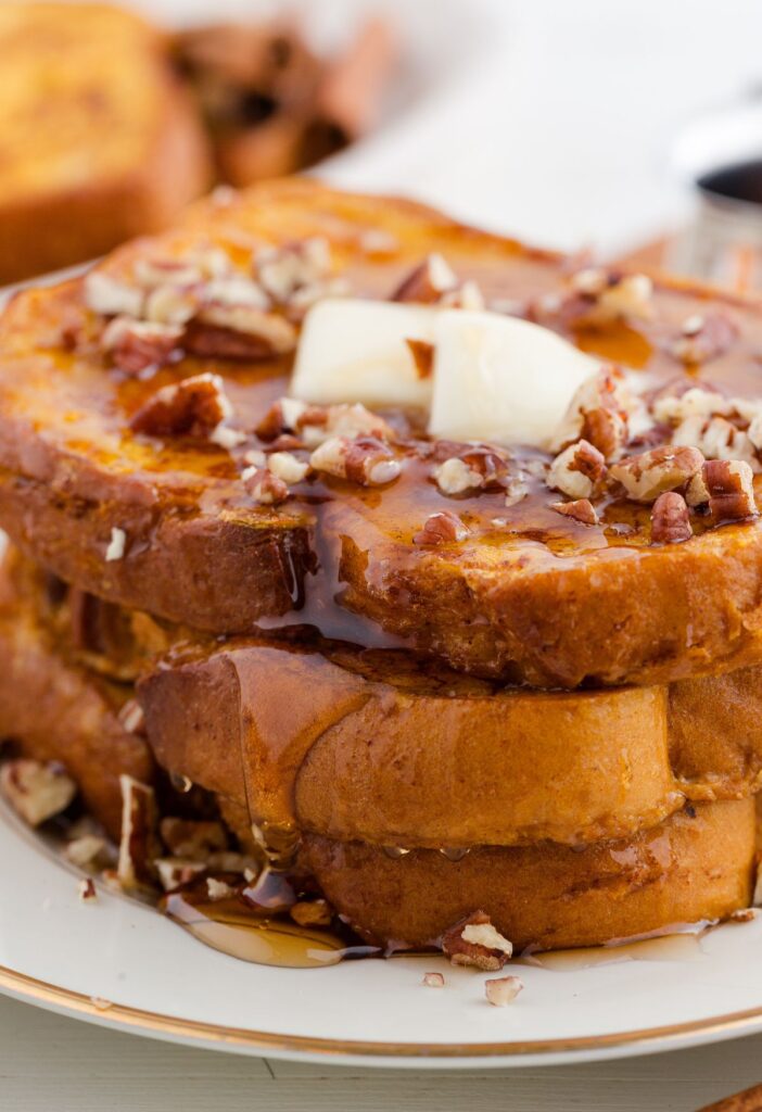 Stack of cooked French toast with butter and syrup on it. 