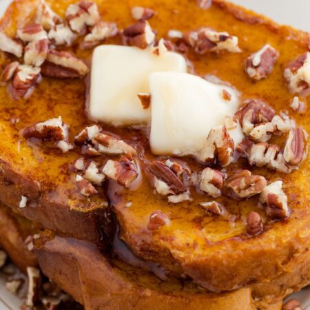 Stack of French toast with butter and pecans on it.