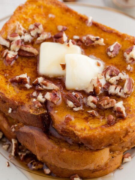 Stack of French toast with butter and pecans on it.