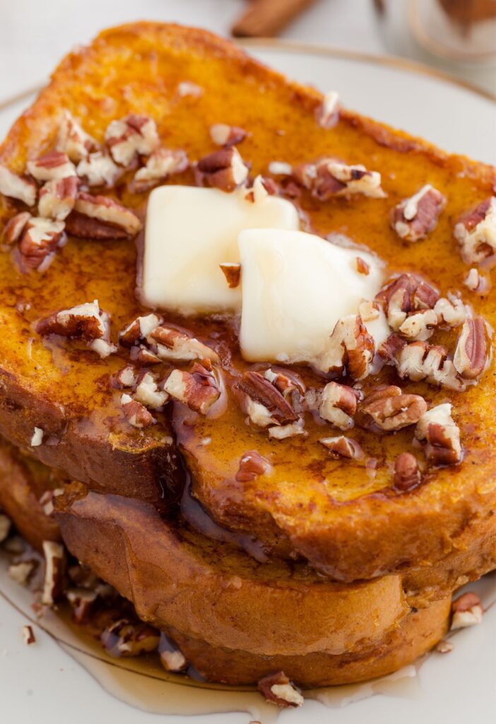 Stack of French toast with butter and pecans on it.