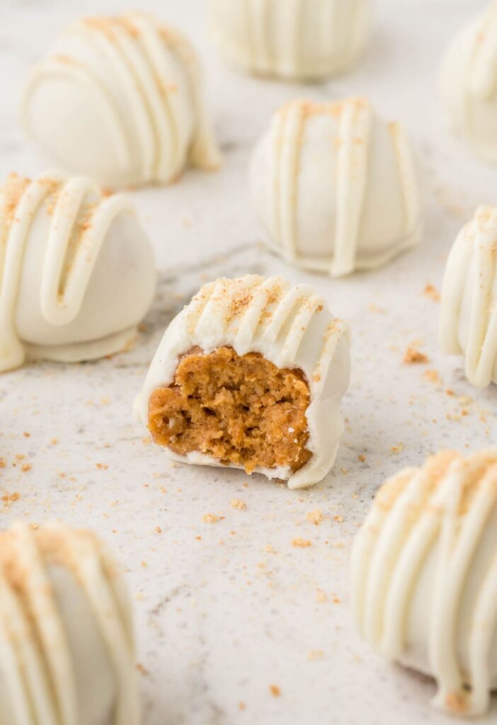 A pumpkin truffle sitting with other truffles on a white background.