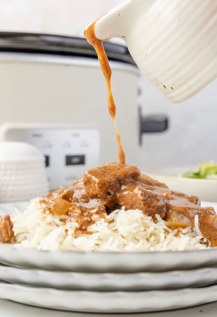 Gravy being poured over top a serving of beef tips and rice. 