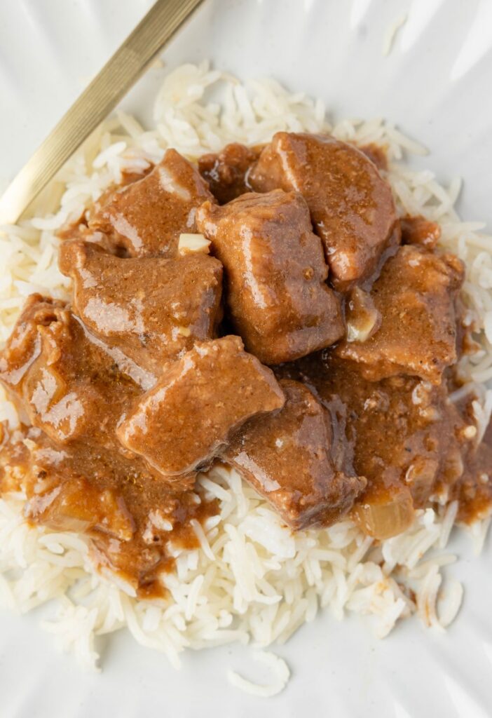 Serving of the beef tips with gravy over top rice and a fork.