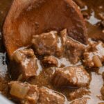 close up of the cooked slow cooker beef with a wooden spoon holding some.