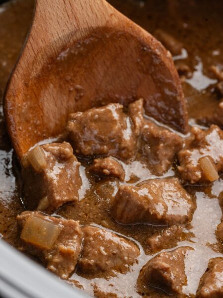 close up of the cooked slow cooker beef with a wooden spoon holding some.