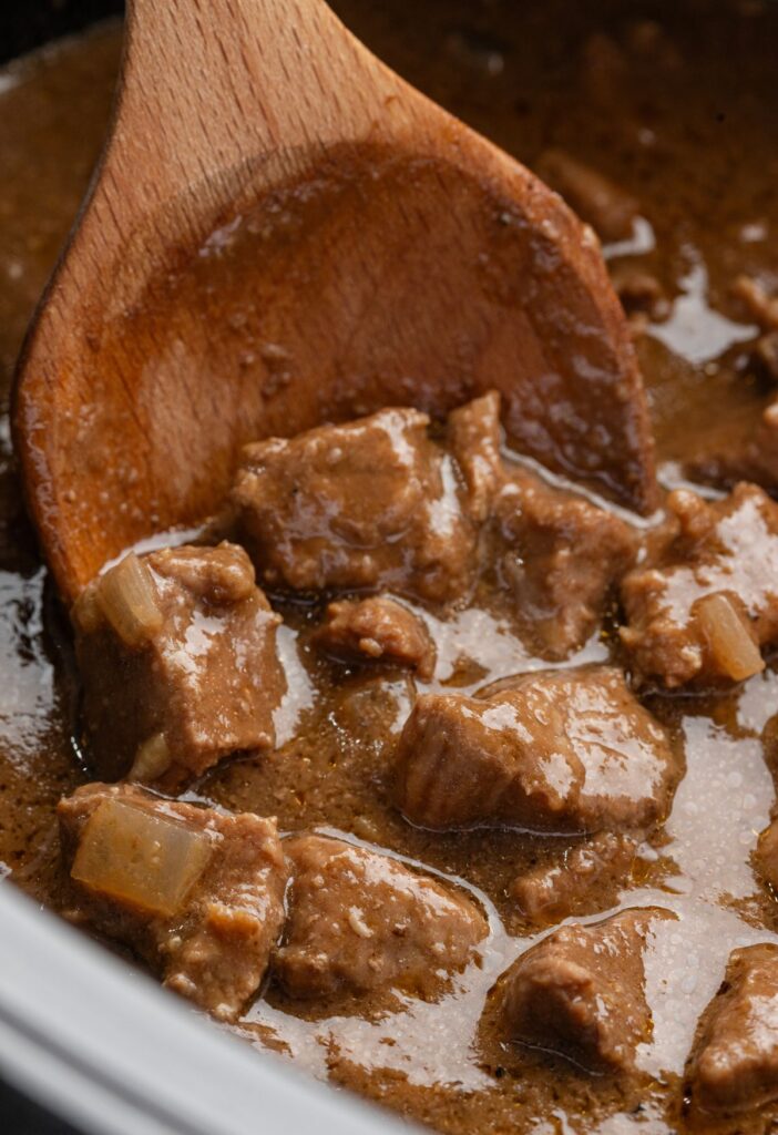 close up of the cooked slow cooker beef with a wooden spoon holding some. 