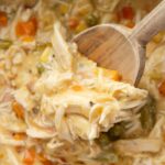 A wooden scoop inside the slow cooker with the cooked chicken pot pie mixture.