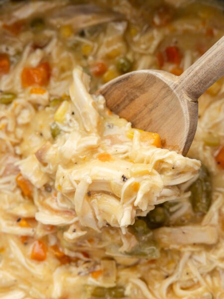 A wooden scoop inside the slow cooker with the cooked chicken pot pie mixture.