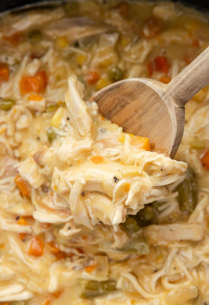 A wooden scoop inside the slow cooker with the cooked chicken pot pie mixture. 