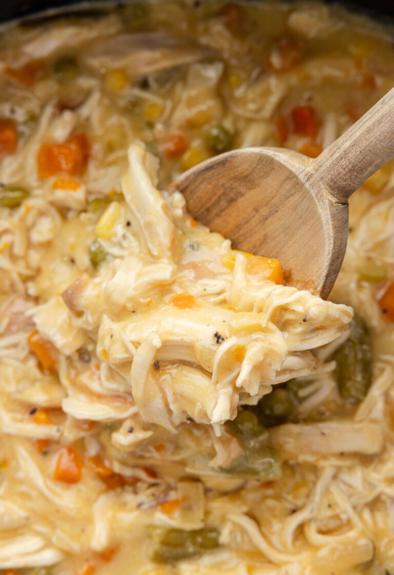 A wooden scoop inside the slow cooker with the cooked chicken pot pie mixture.