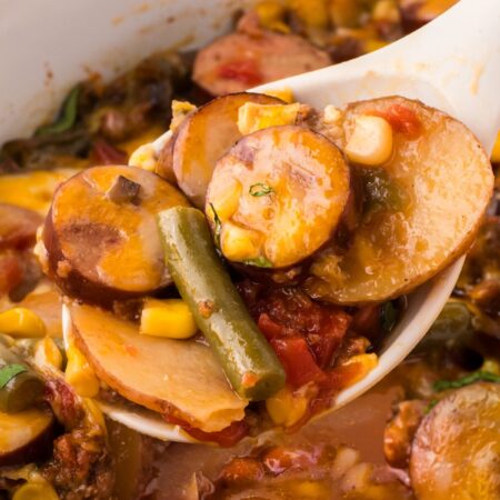 A spoon with some casserole on it above the slow cooker