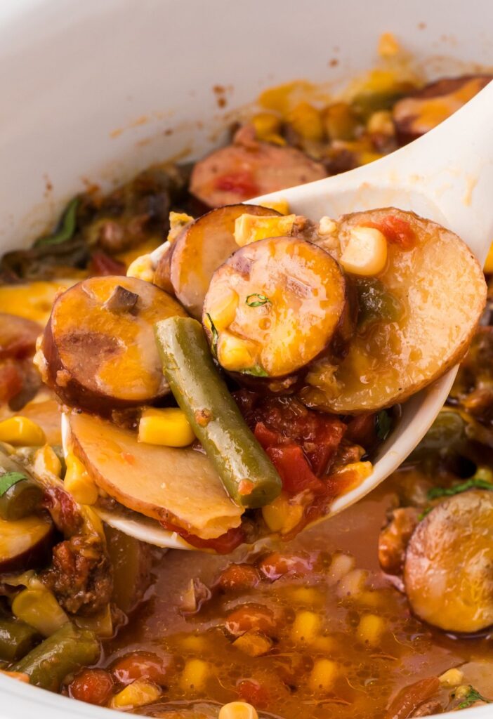 A spoon with some casserole on it above the slow cooker