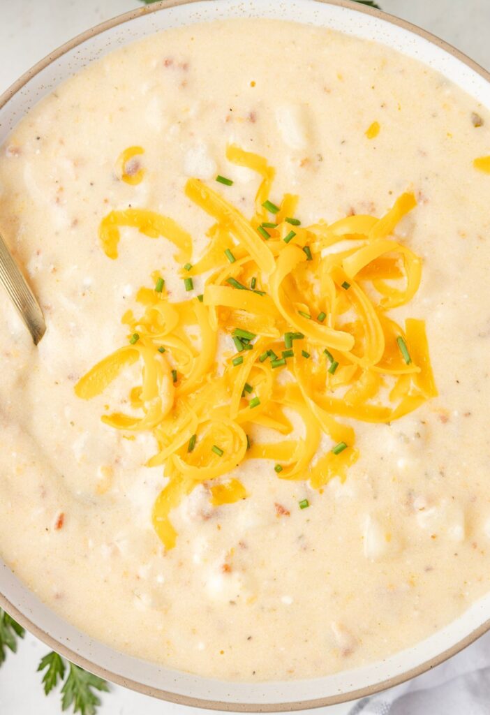 A bowl of potato soup with cheese on it and a spoon inside the bowl of soup. 