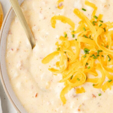 A bowl of soup with a spoon and shredded cheese on top