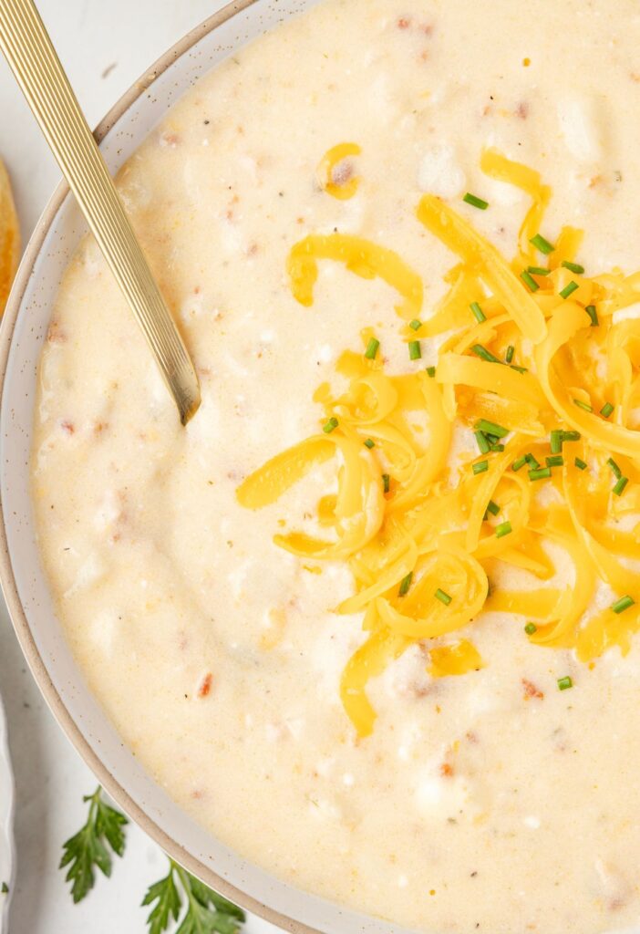 A bowl of soup with a spoon and shredded cheese on top