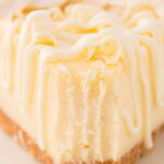 A front view of a slice of cheesecake with a fork bite taken out of the front