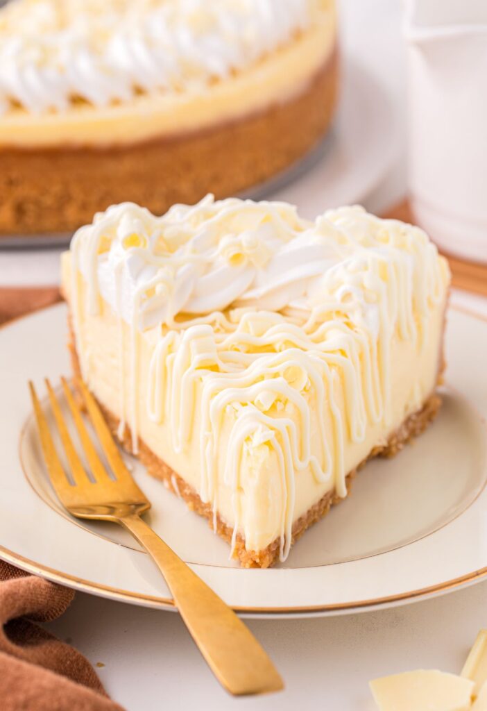 A slice of cheesecake with white chocolate on a white and gold plate with a fork on it