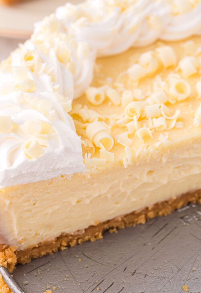Side view of the cheesecake with white chocolate curls, graham cracker crust, and whipped cream. 