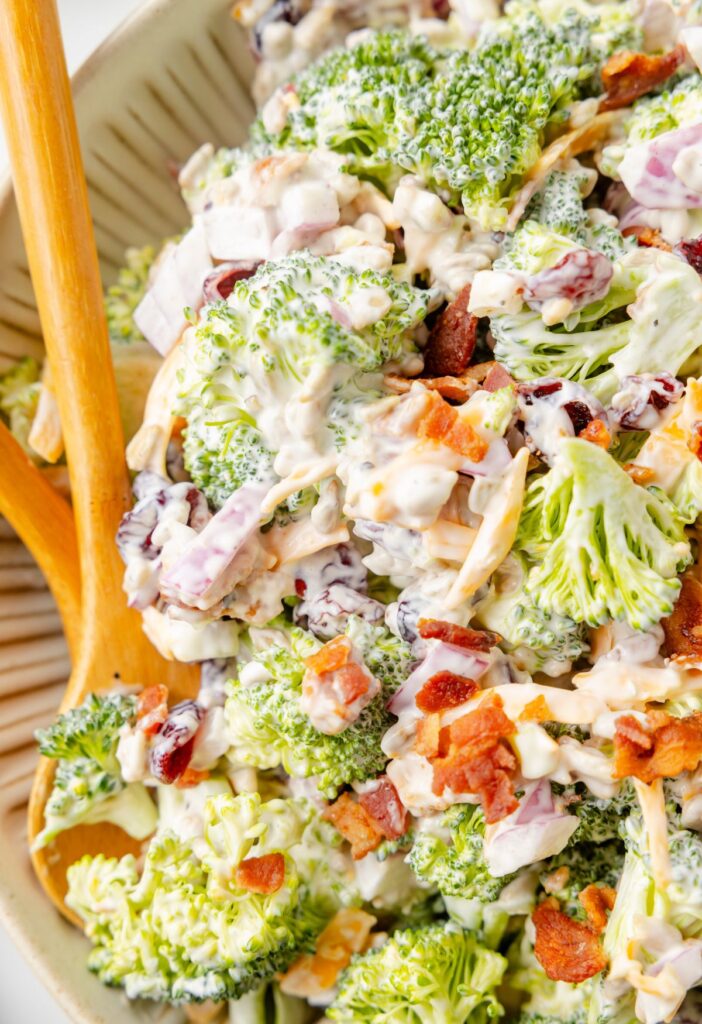 Close up of the broccoli salad inside a serving bowl with a wooden spoon. 