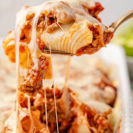 A spoon with with stuffed shells on it and a cheese pull
