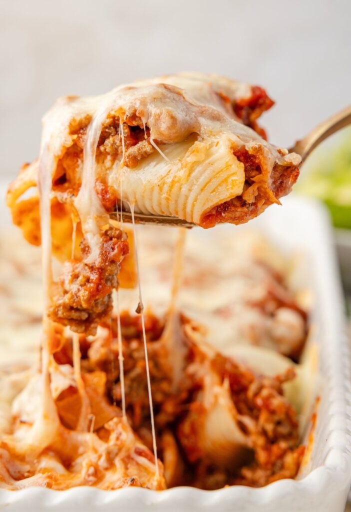 A spoon with with stuffed shells on it and a cheese pull 