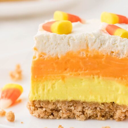 A slice of lush dessert with candy corn colors on a white plate.