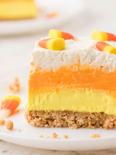 A slice of lush dessert with candy corn colors on a white plate.