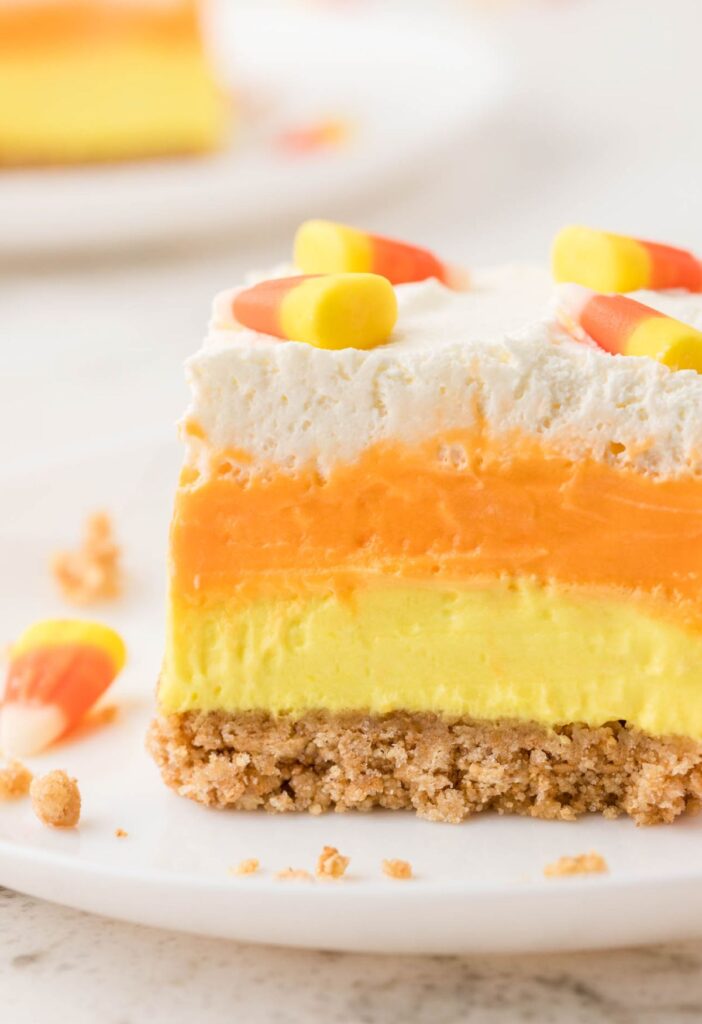 A slice of lush dessert with candy corn colors on a white plate.