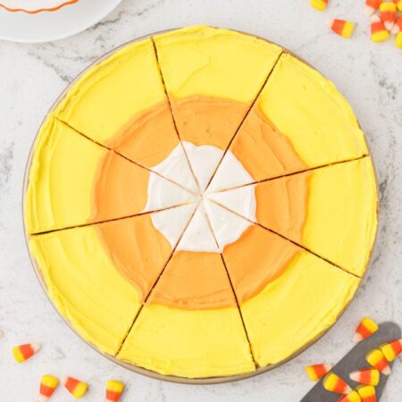 A sliced cookie pizza with candy corn colors and candy to the side.