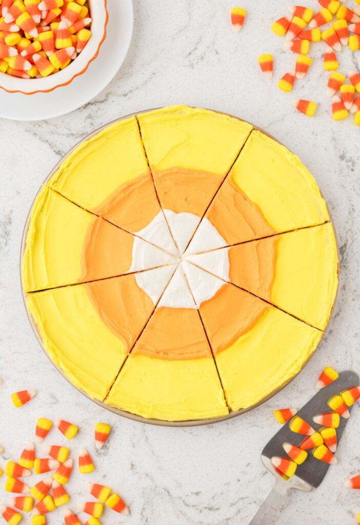 A sliced cookie pizza with candy corn colors and candy to the side.