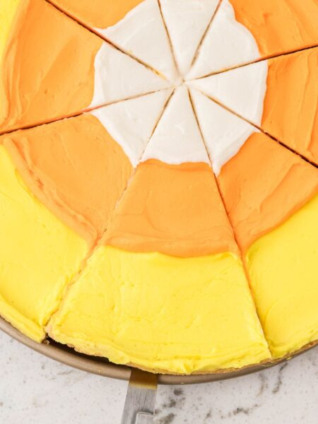 A dessert pizza with candy corn colors cut into slices.